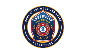 Circular logo for Edgewater Volunteer Fire Dept. Features a firefighter helmet with "Rescue", "EMS", and "Fire" written on it. Text around the logo reads "Home of the Woodland Beach Volunteers.